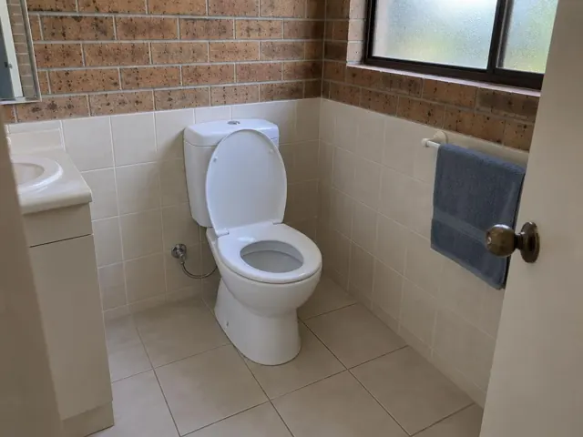 Clean white toilet in a tiled bathroom with towel rail and sink vanity in Doonside
