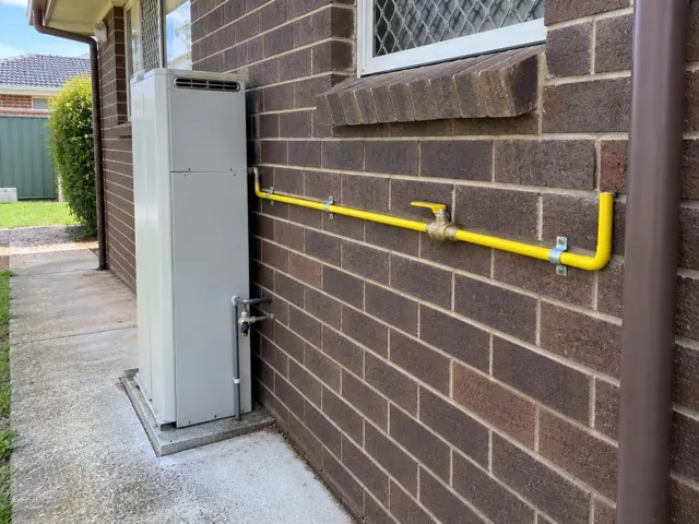 Yellow gas pipe and meter on a brick exterior wall beside a house window in Doonside